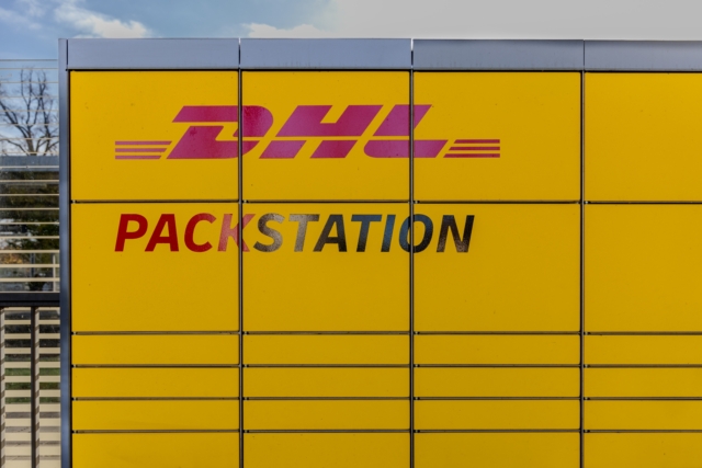 A bright yellow DHL Packstation parcel locker outdoors, with the DHL logo and 